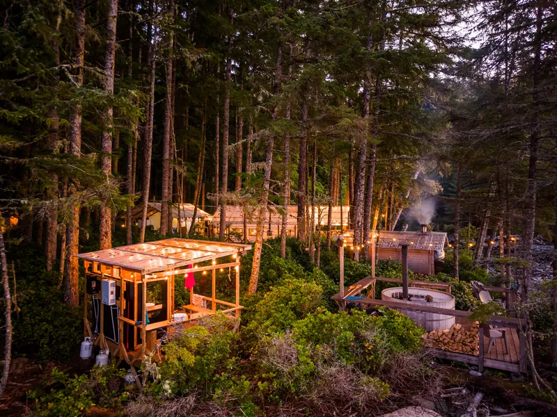 At dusk, string lights glow among the trees at Orca Camp, and smoke rises from a chimney beside the wood-fired hot tub.