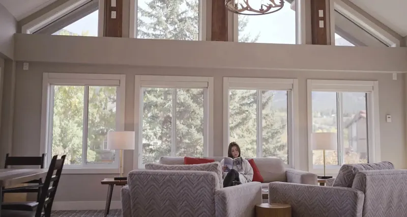 A guest reads in a bright lounge with tall windows and grey sofas.