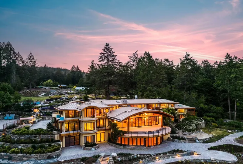From the air at dusk, the Lightwater Cove house glows among terraced gardens and tall trees.