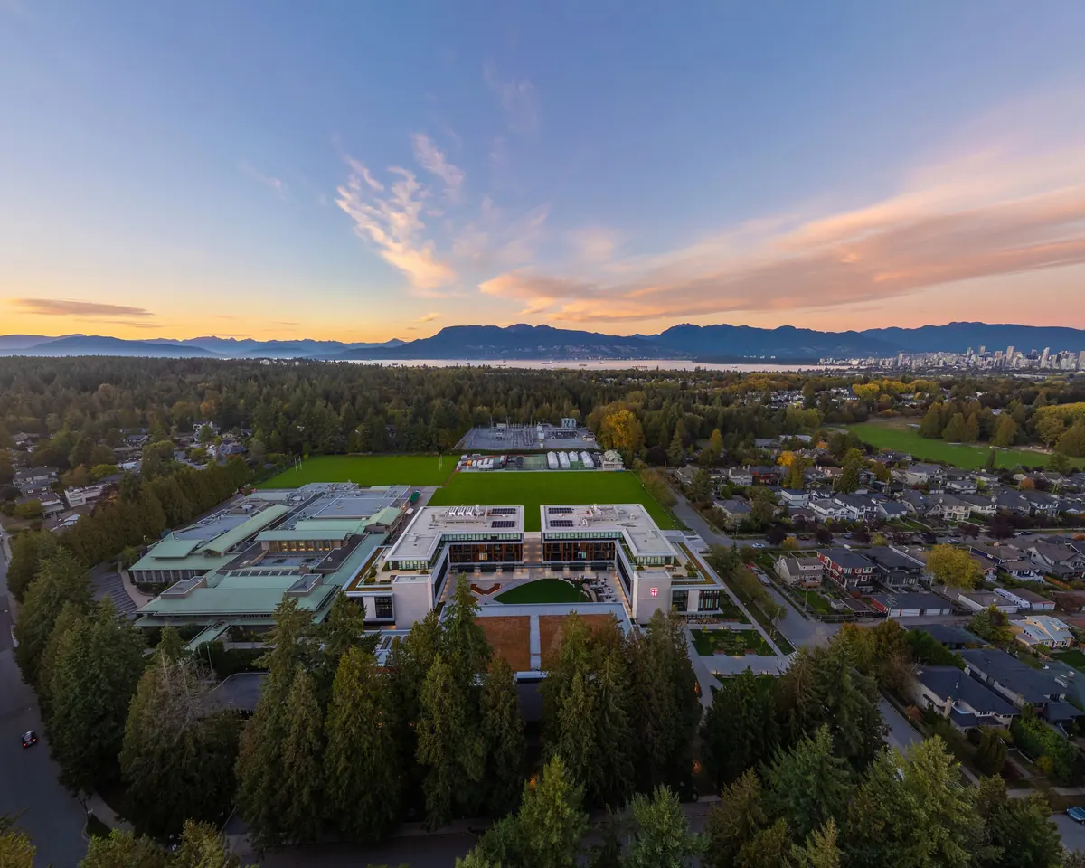 Seen from the air at sunset, the new senior school sits among tall evergreens, and the city and the North Shore mountains rise beyond it.