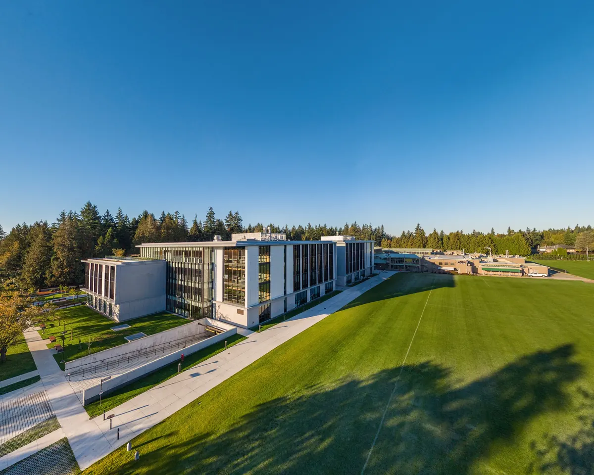 The glass and white stone front of the new senior school rises above a sloping green field.