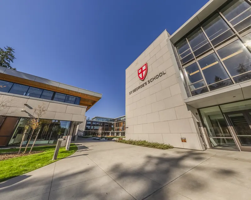 The school’s name and red crest stand on a pale stone wall beside the glass front of the new senior school.