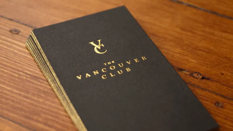 A stack of the club’s black business cards shows the VC monogram and the club’s name in gold foil on a wooden table.