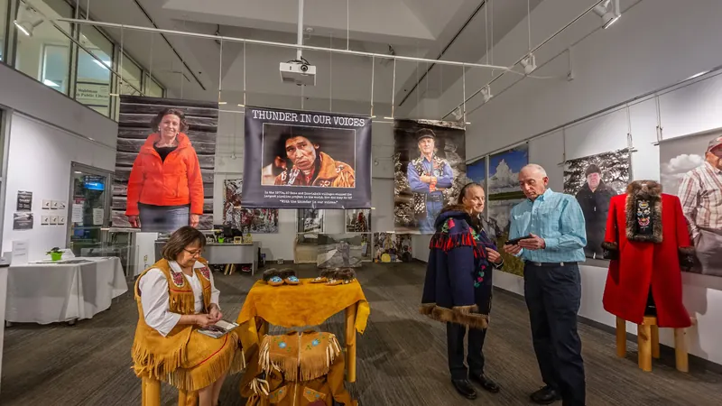 Large photographic portraits hang around the white walls of the gallery, and visitors gather in the middle of the room.
